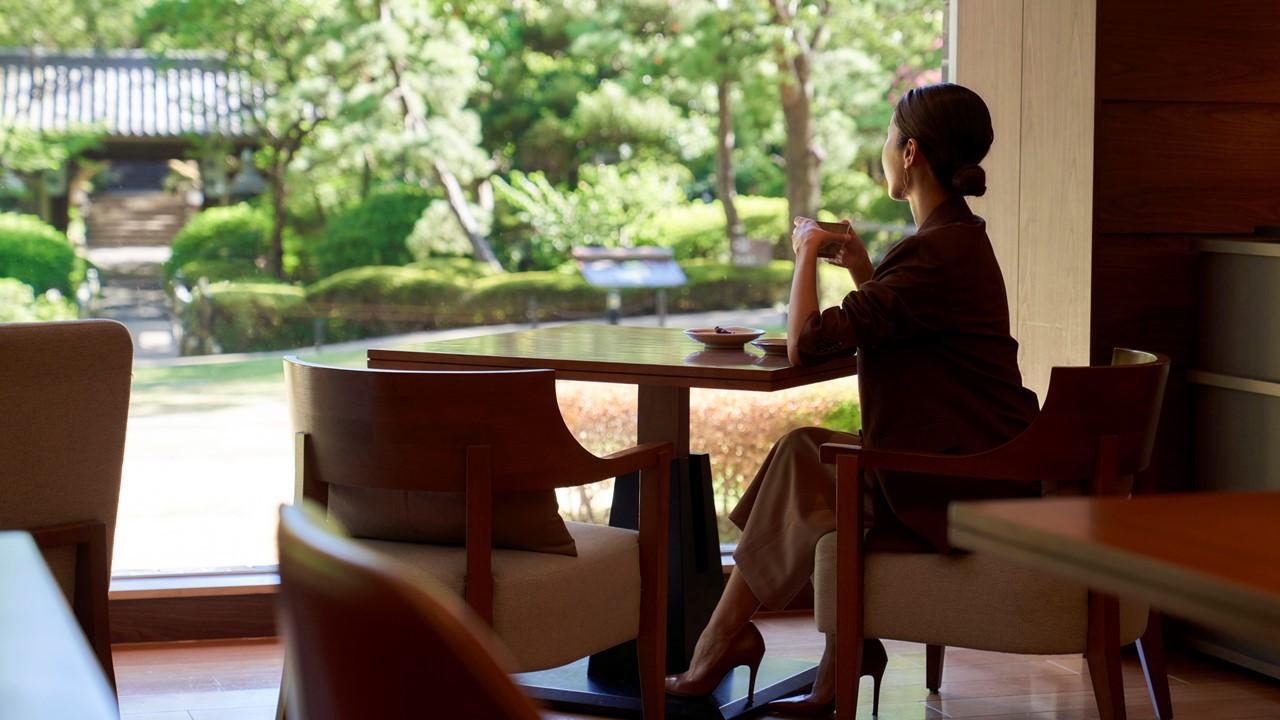 グランドプリンスホテル高輪「クラブラウンジ 花雅」で女性がお茶をしながら庭園を眺めている。