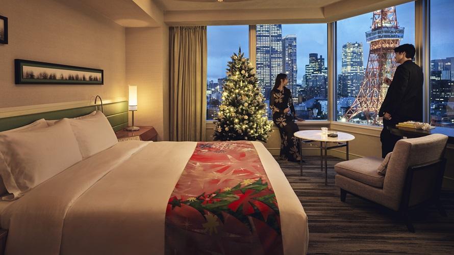 東京タワーをバックに、クリスマスツリーの飾られた客室でくつろぐカップル。